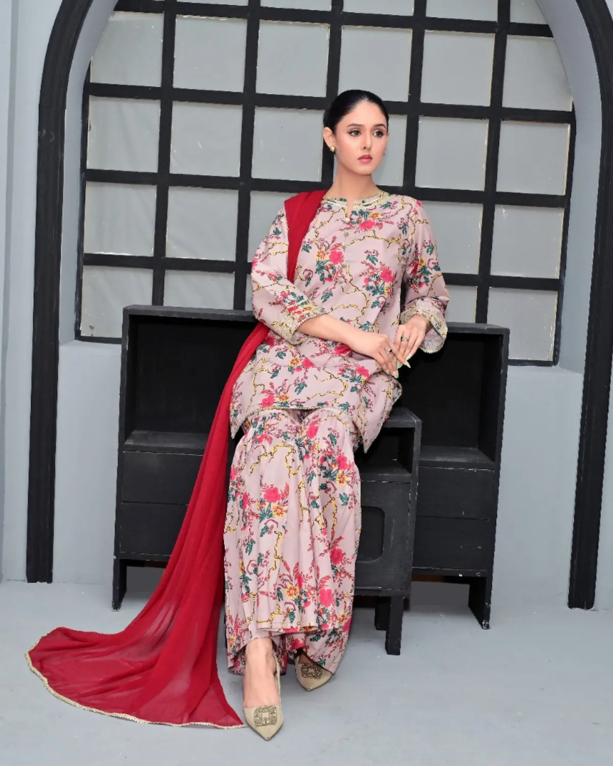 Woman in a floral outfit with a red dupatta sitting on a black bench.