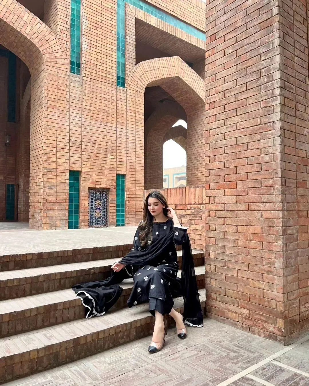 Woman sitting on steps in front of a brick building with arches