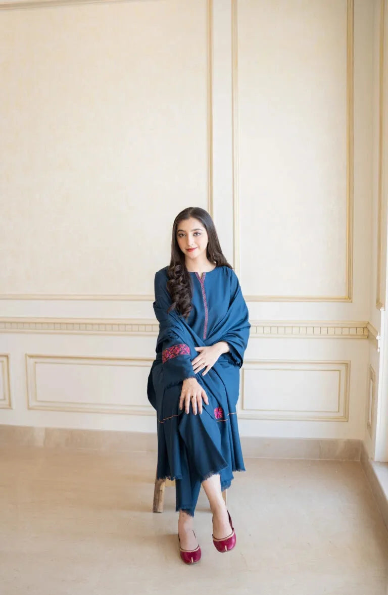 Woman in a blue dress sitting on a chair against a beige wall.