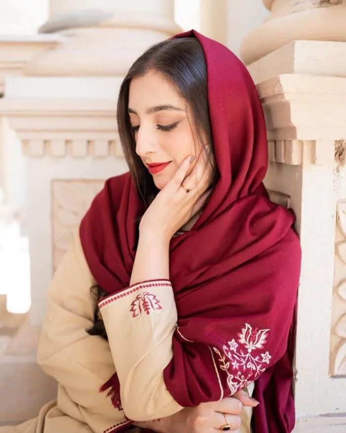 Woman wearing a red hijab with embroidery, sitting indoors.