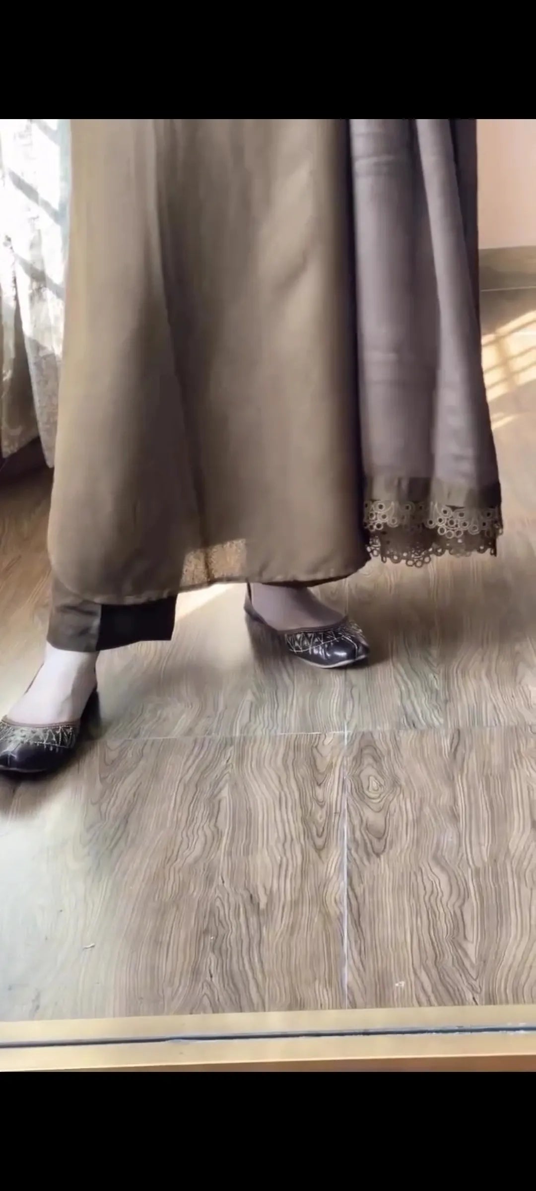 Person wearing a long beige skirt and black shoes on a wooden floor.