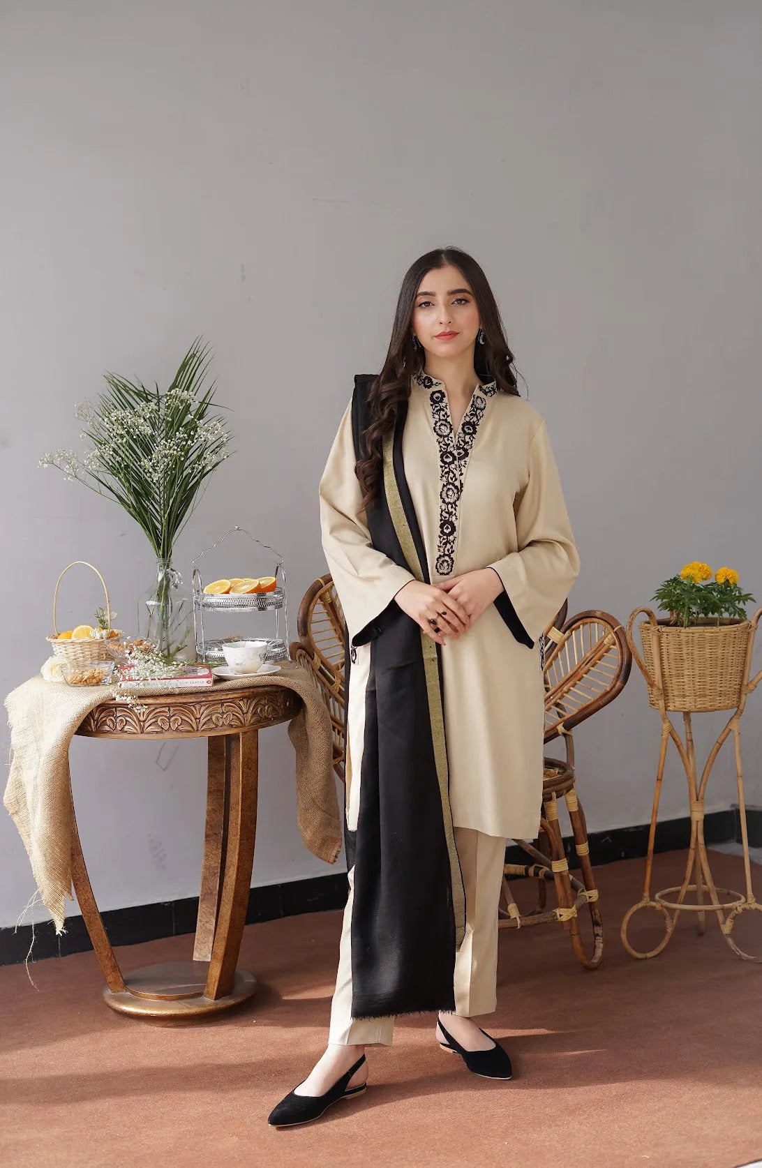 Woman in a beige and black traditional outfit standing in a room with decorative elements.