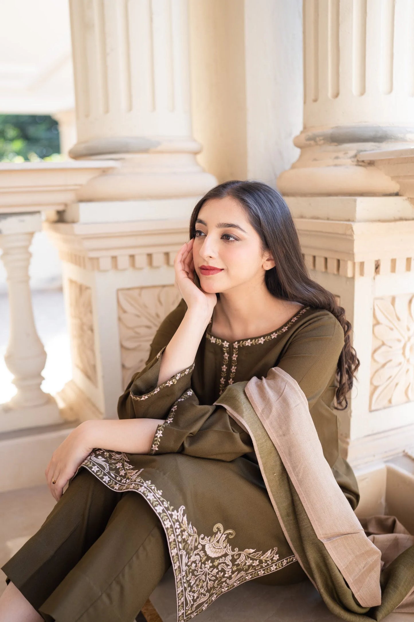 Woman in traditional outfit sitting on a stone bench with classical architecture in the background