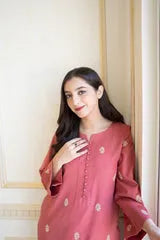 Woman wearing a red traditional outfit with gold buttons against a white wall.