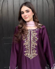 Woman wearing a purple embroidered dress standing in front of a dark wooden door.