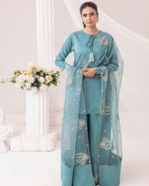 "Teal blue Pakistani designer three-piece suit for women – formal stitched outfit with embroidered chiffon dupatta, straight shirt, and wide-leg trousers. Elegant festive and Eid dress with silver floral embroidery, styled with pearl tassels and statement earrings – luxury Pakistani fashion 2025."