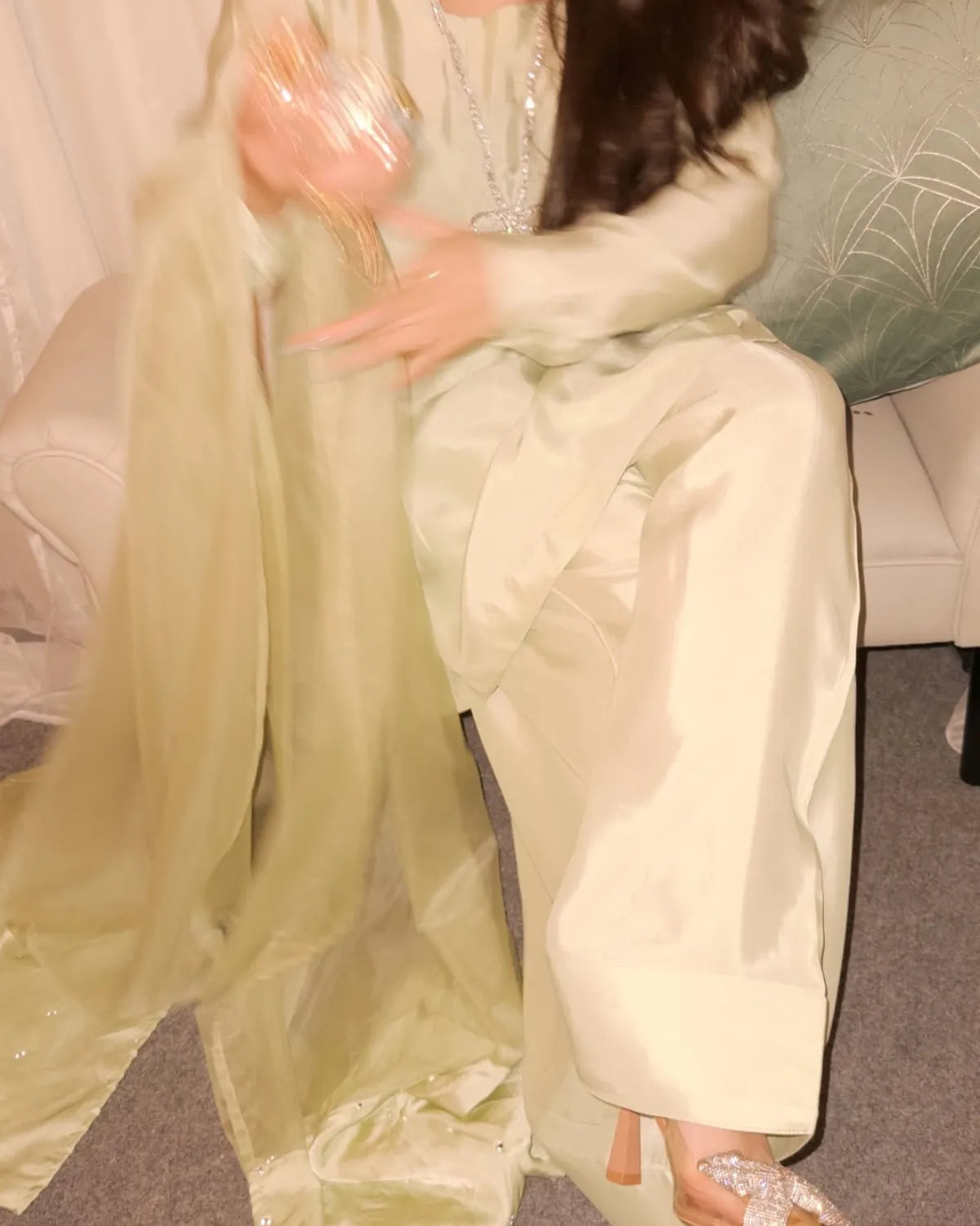 Person wearing a light-colored outfit with a sheer overlay sitting on a couch.