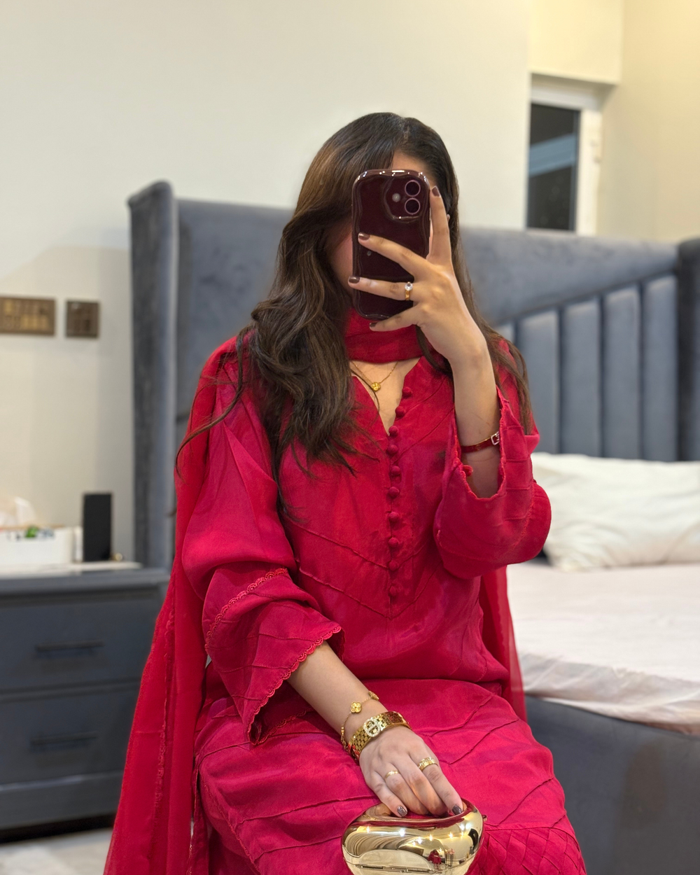 Person wearing a red outfit sitting on a bed in a bedroom.