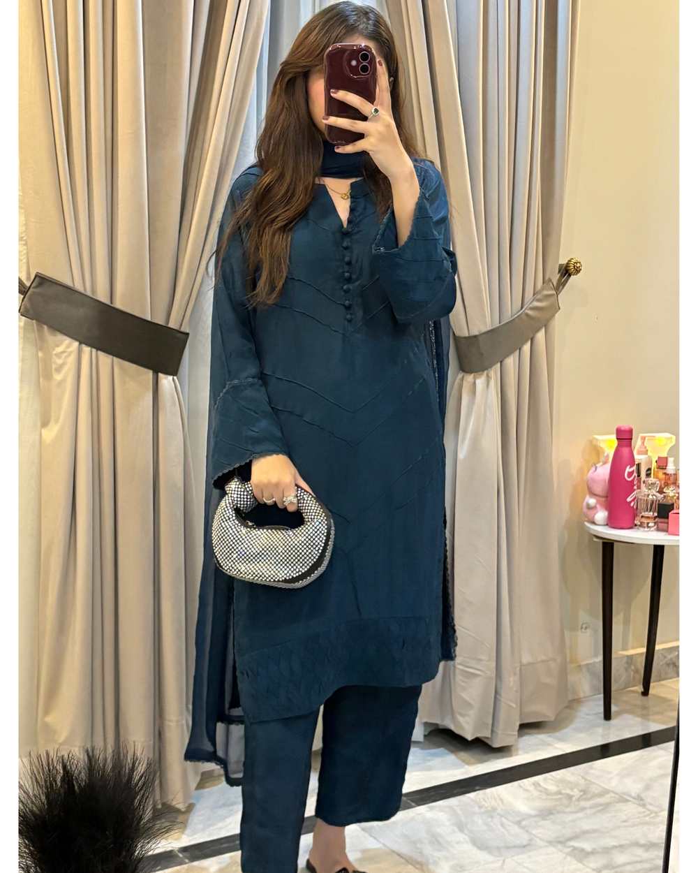 Woman taking a mirror selfie wearing a teal outfit with a patterned handbag indoors.