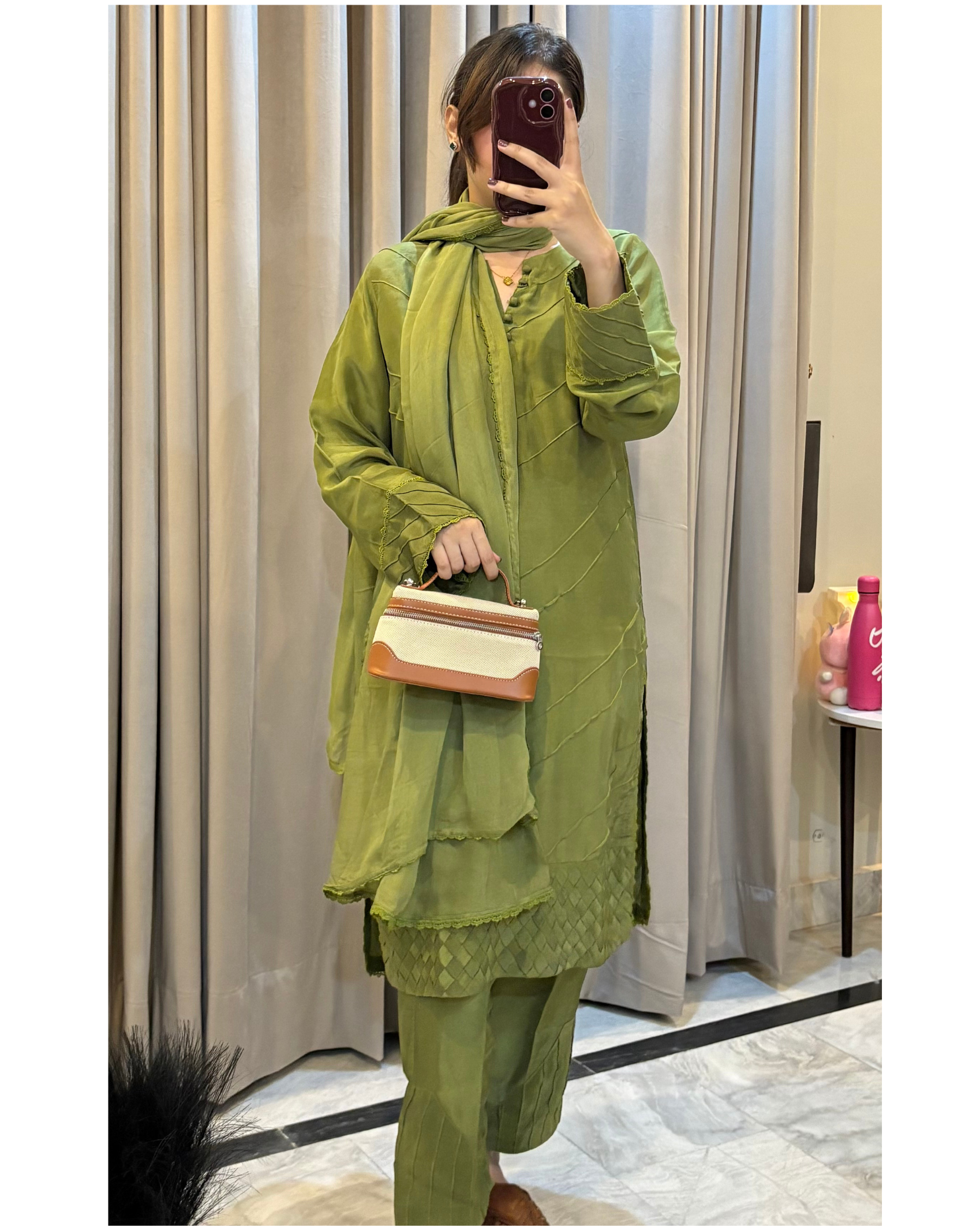 Person wearing a green outfit with a matching handbag, standing in front of a curtain.