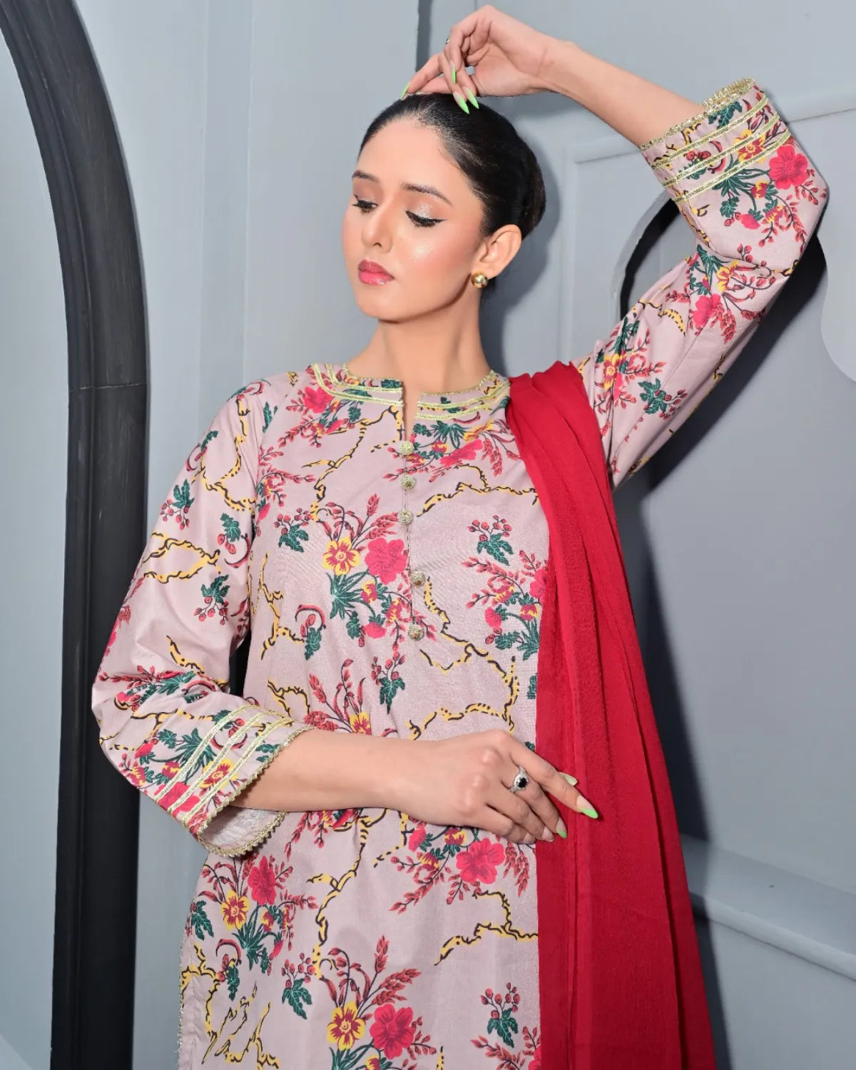 Woman wearing a floral dress with a red dupatta in front of a mirror.