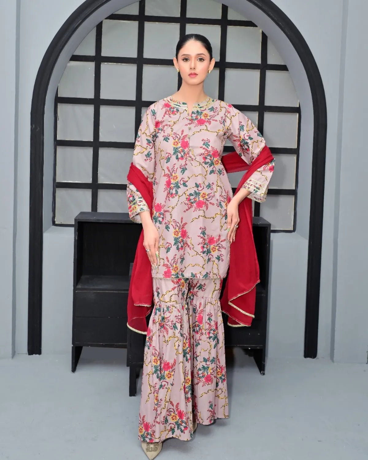 Woman in a floral dress with a red shawl standing in front of an archway.