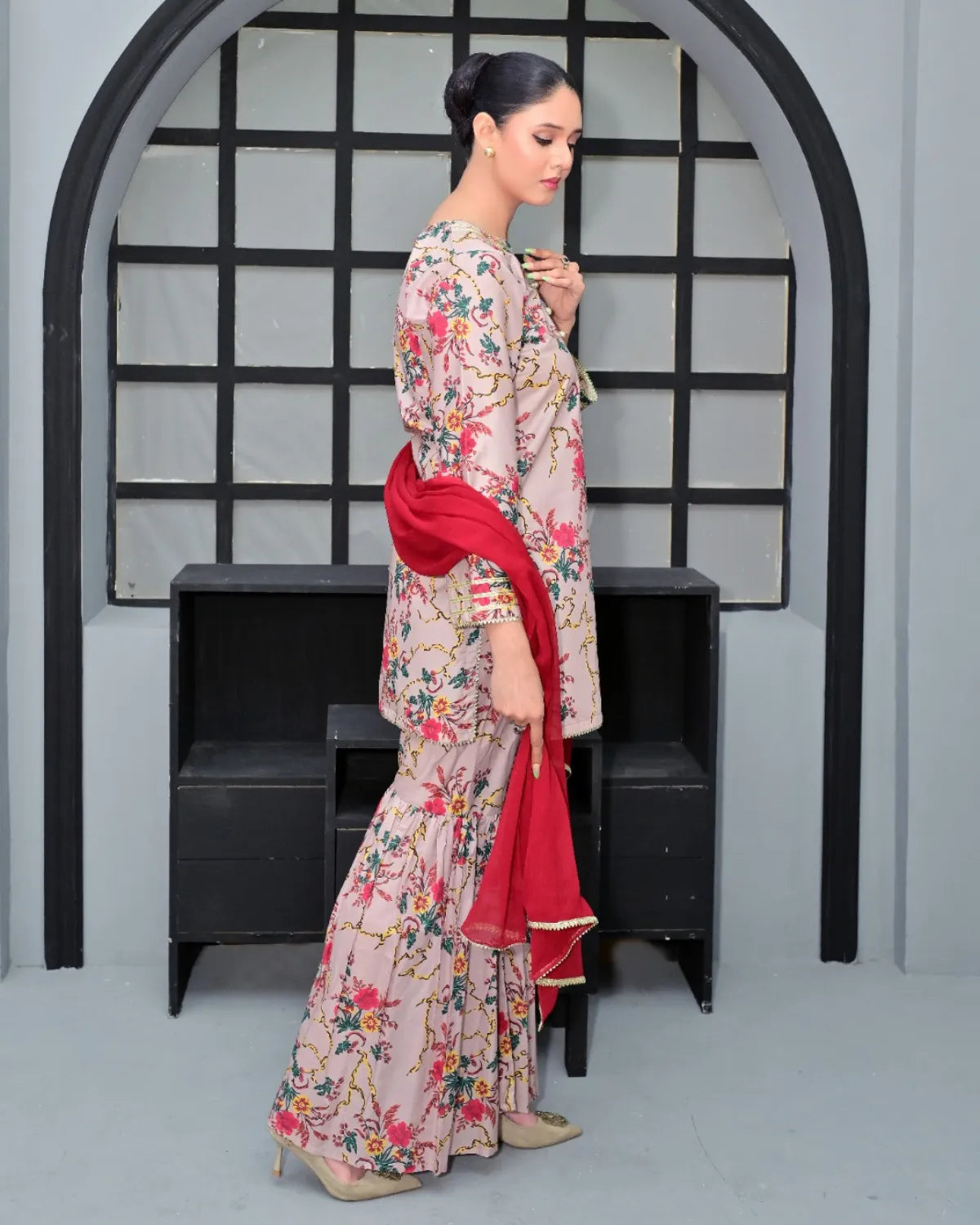 Woman in a floral dress with a red dupatta standing in front of a black and white geometric arch.