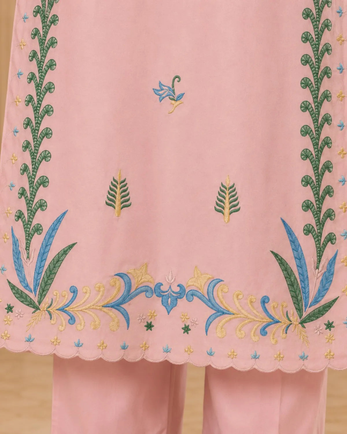 Embroidered pink fabric with green and blue floral patterns on a wooden surface