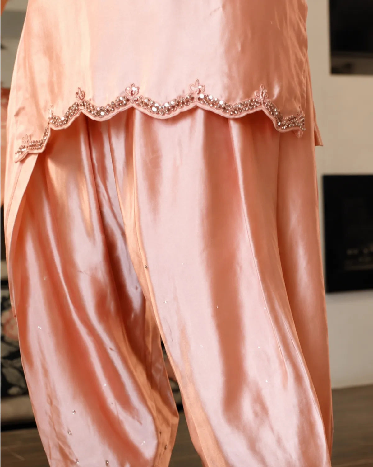 A close-up of peach-colored satin harem pants with a decorative scalloped border embellished with sequins and beads.