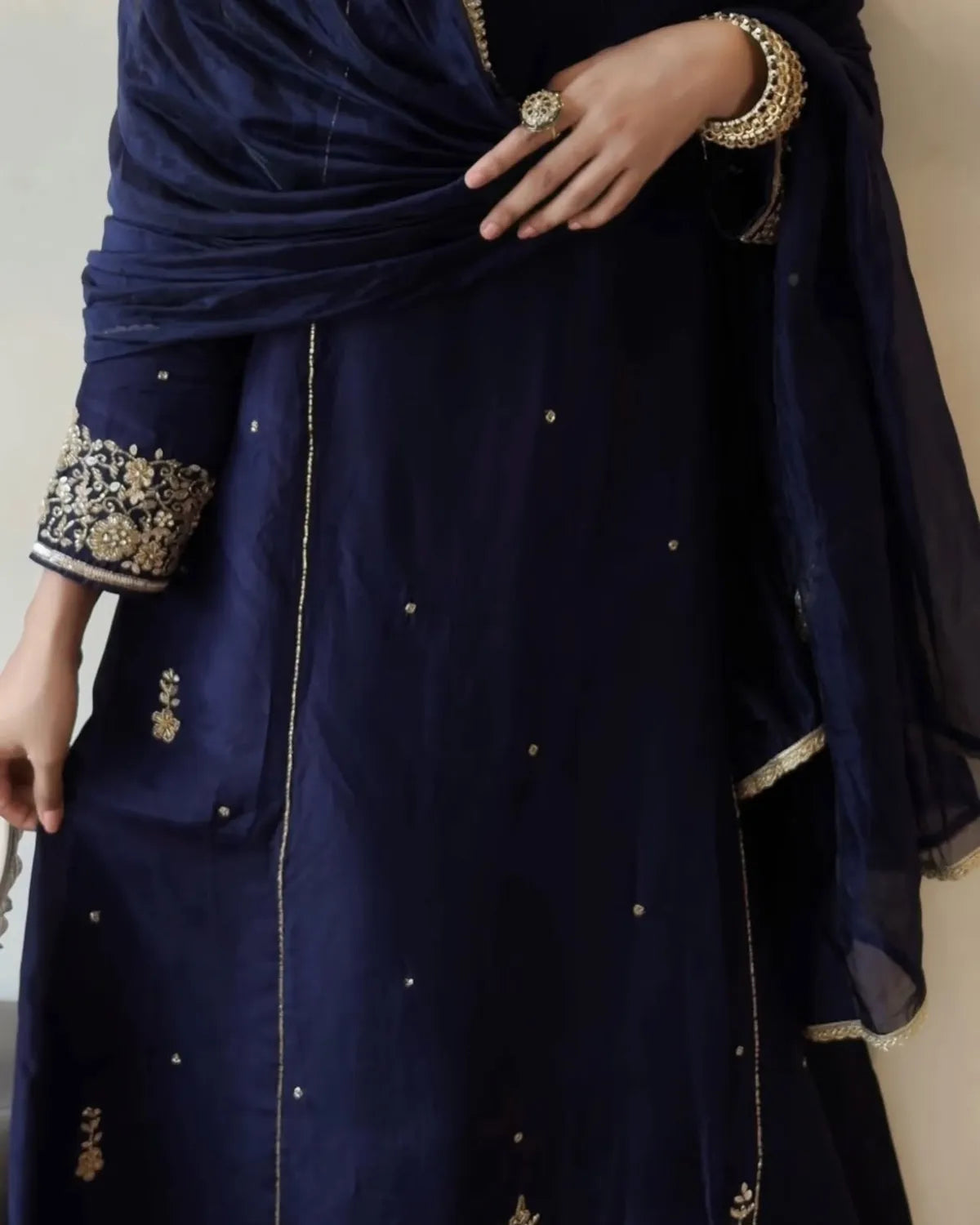 A close-up of a navy blue traditional outfit with gold embroidery on the sleeve cuffs and scattered small gold motifs on the fabric, worn with a matching sheer dupatta.