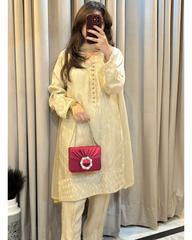 Person wearing a light-colored outfit with a red handbag in front of beige curtains.