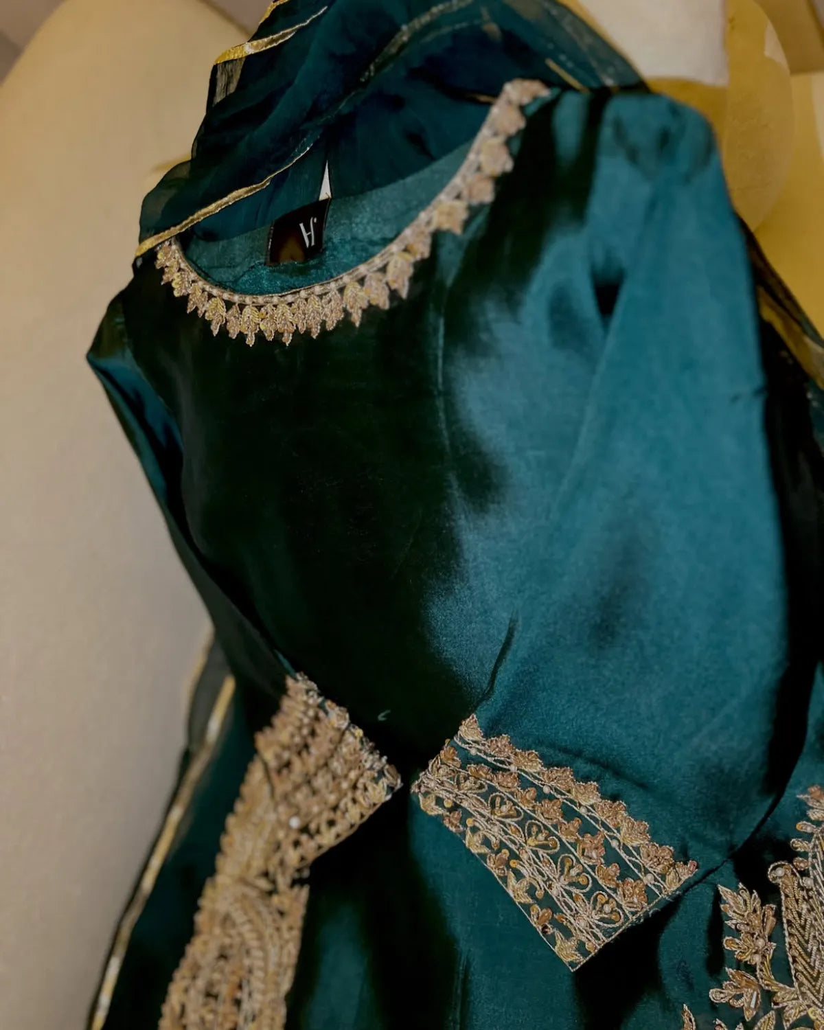 A dark teal green embroidered fabric garment, likely a traditional kurta or dress, featuring intricate gold and silver beadwork and embroidery around the neckline and sleeve cuffs, shown against a neutral background.
