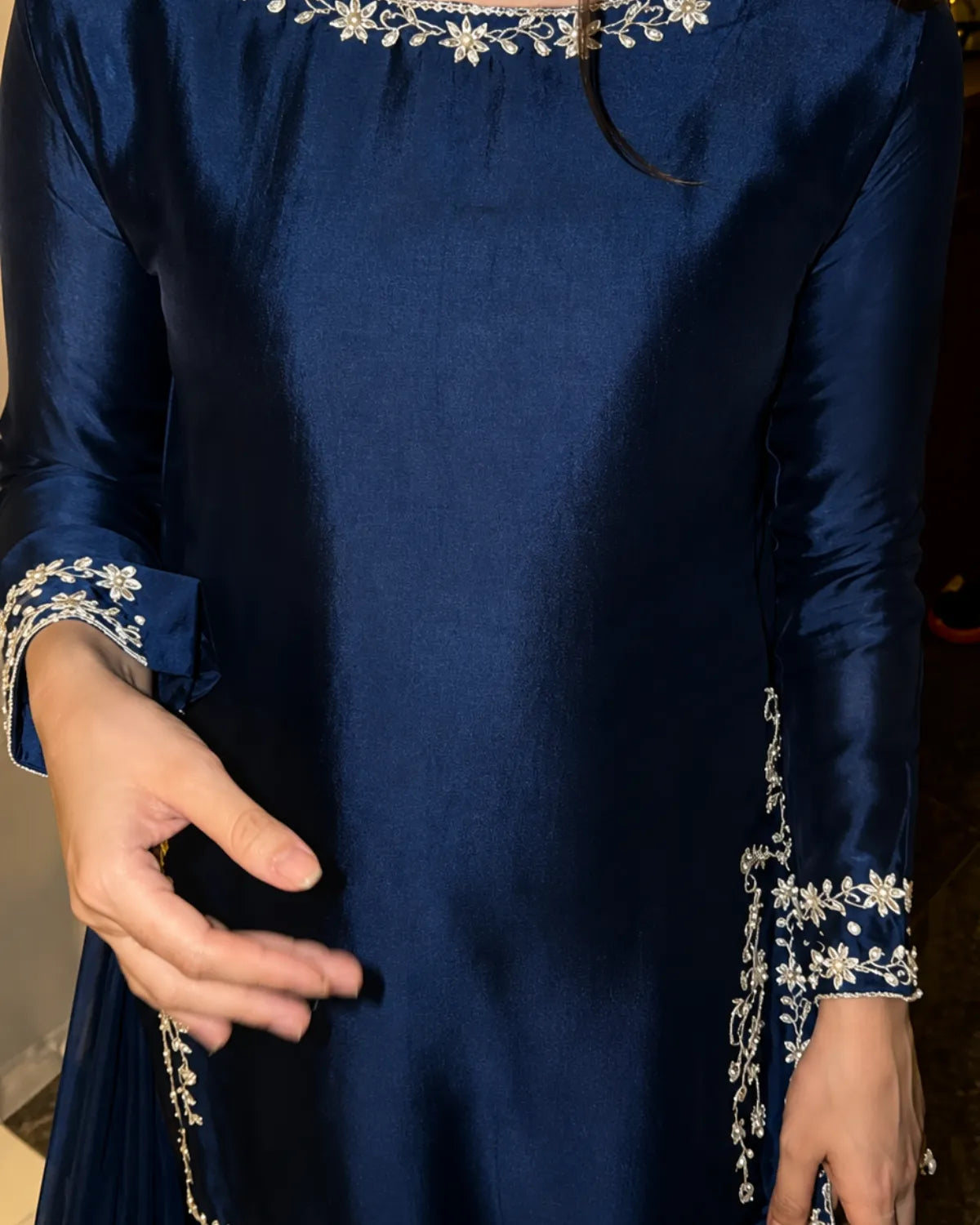 A close-up of a navy blue satin kurta with white floral embroidery on the neckline, cuffs, and hem, worn by a model.