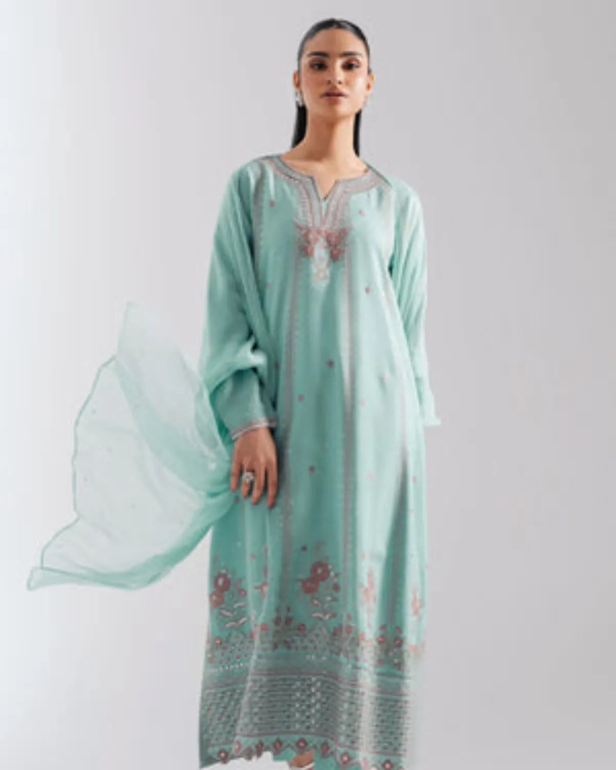 A woman modeling a mint green traditional long kurta with pink floral embroidery and a matching sheer dupatta, set against a plain light gray background.