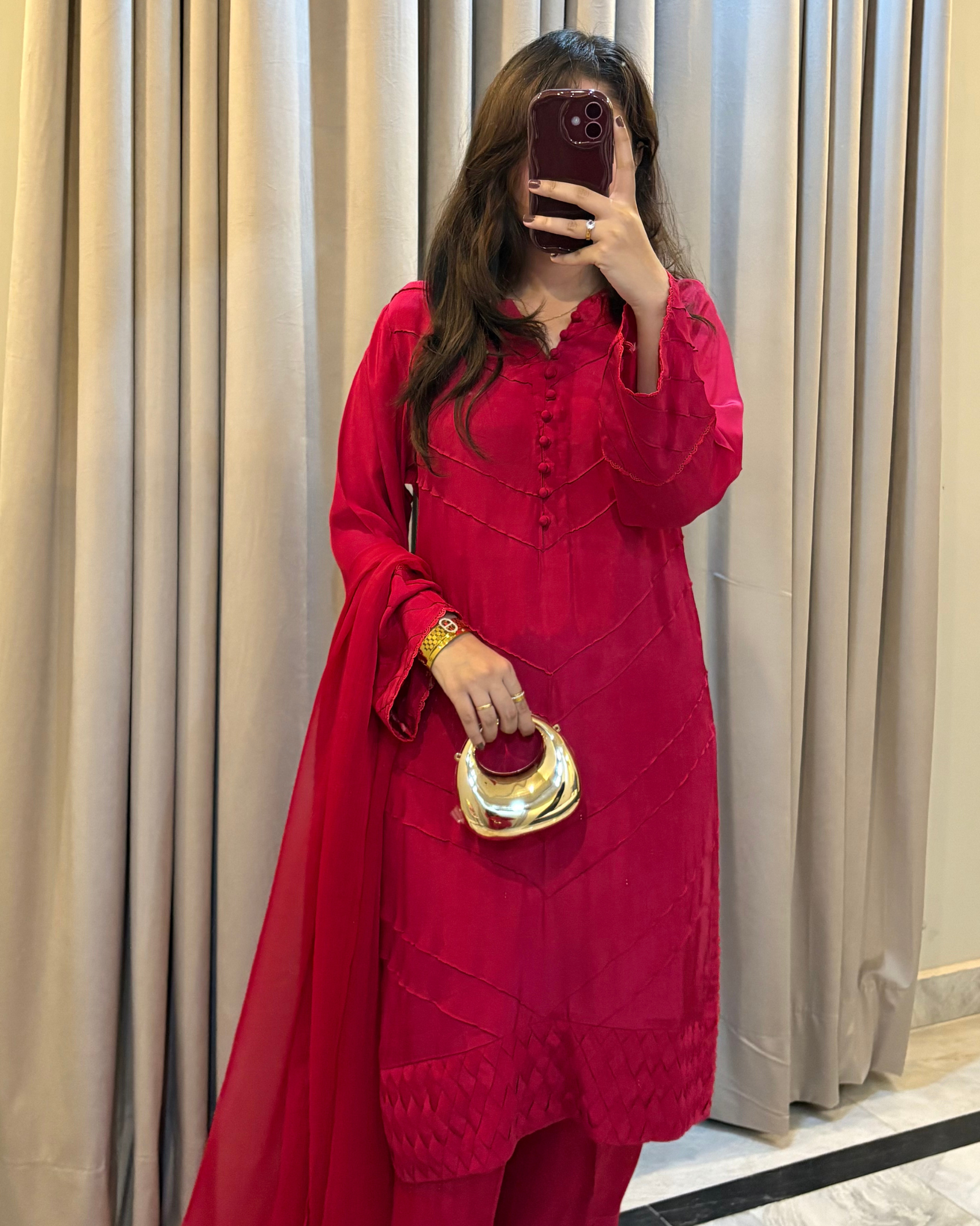 Person wearing a red outfit with a gold handbag in front of beige curtains