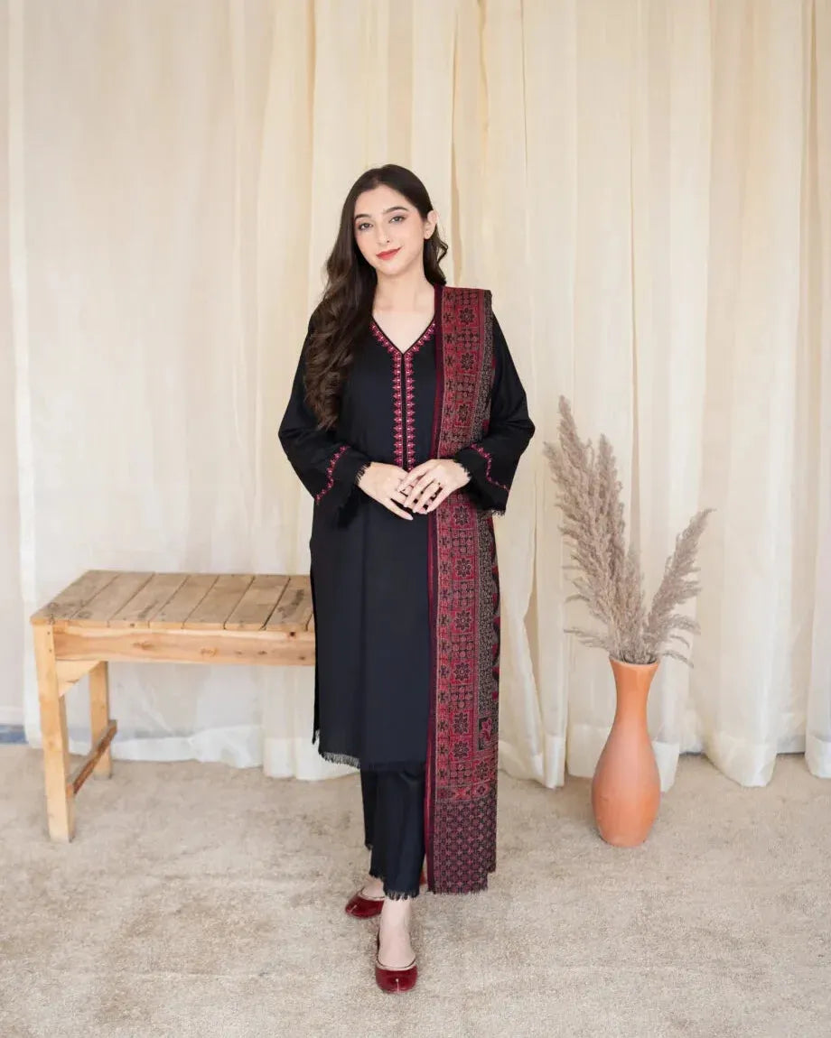 Woman wearing a black and red traditional outfit standing in a room with a wooden bench and vase.