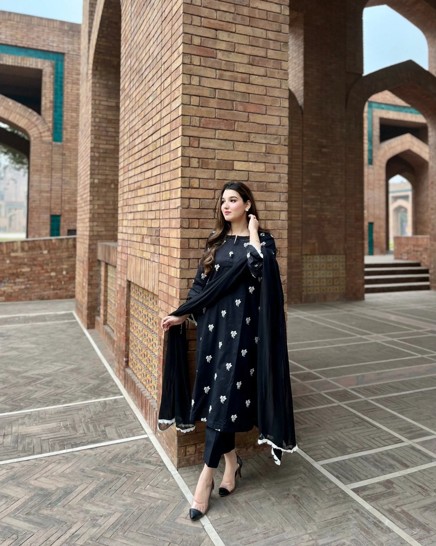 Woman in a black outfit with white patterns standing in front of a brick building.