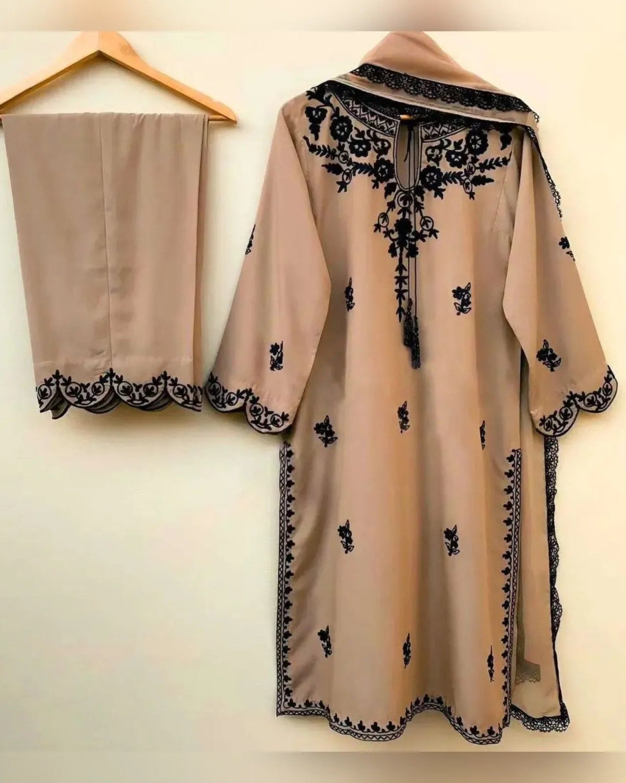 Beige dress with black embroidery on a hanger against a white background