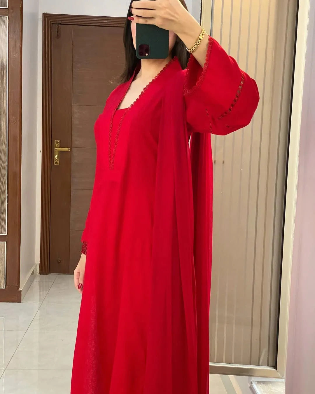 Person wearing a red dress standing in a room with a wooden door and tiled floor.