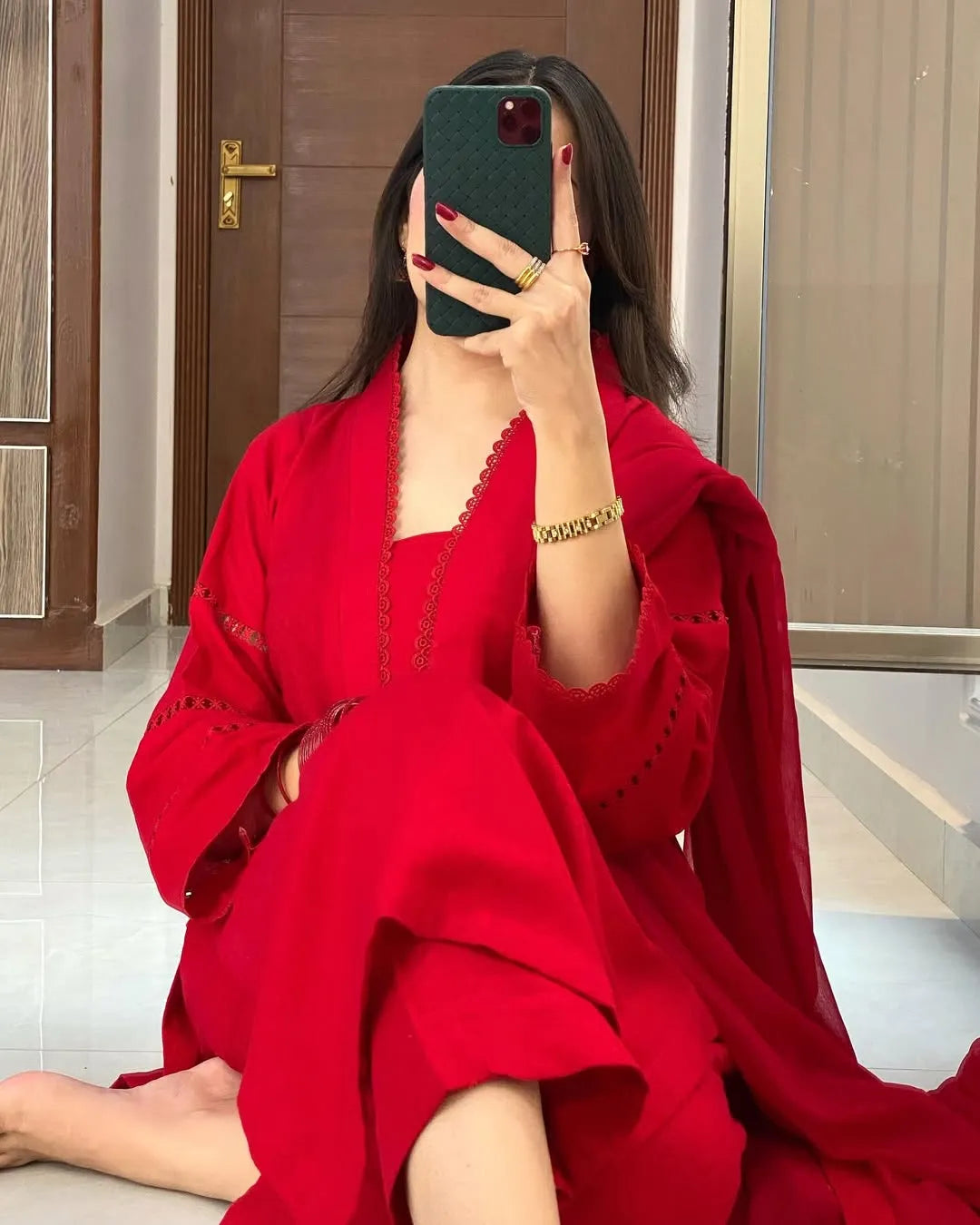 Person wearing a red dress sitting on the floor with a phone in hand.