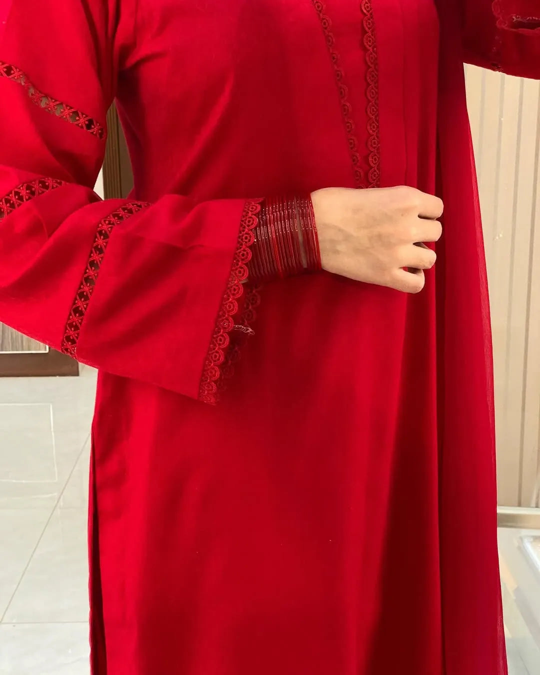 Red dress with intricate detailing on sleeves and hem, held by a hand.