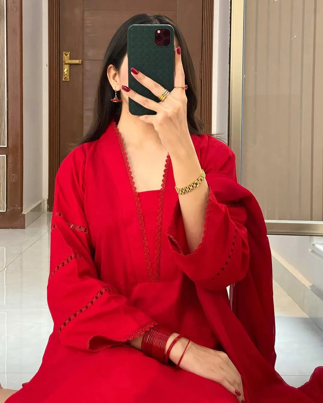 Person wearing a red outfit with gold accents, sitting indoors.