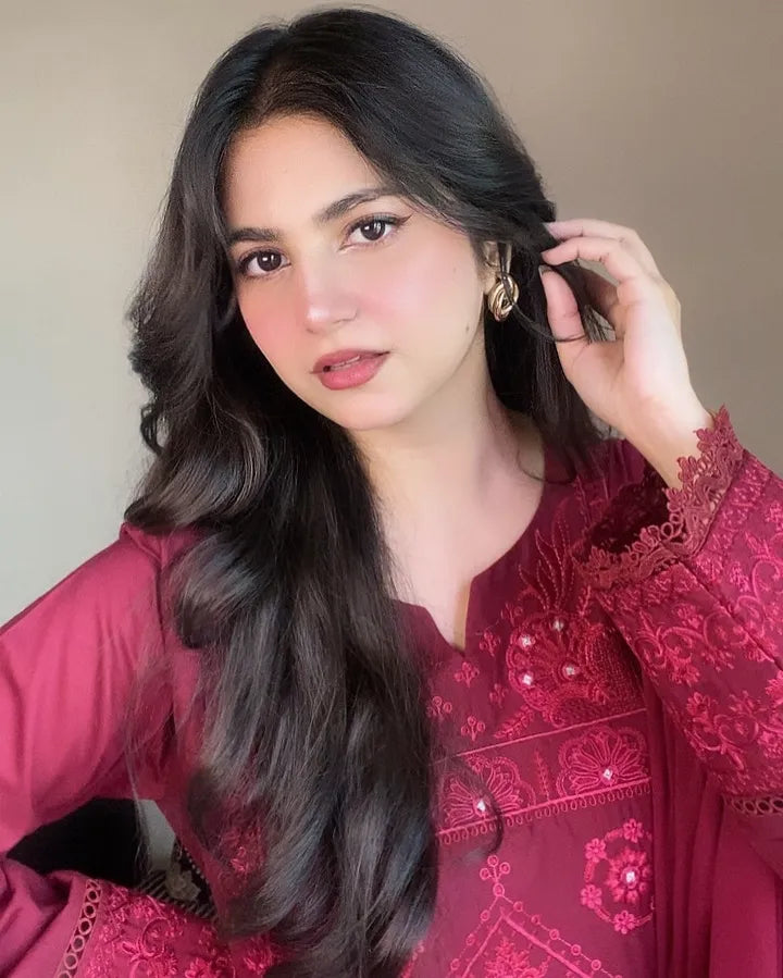 Woman with long dark hair wearing a red embroidered outfit against a neutral background
