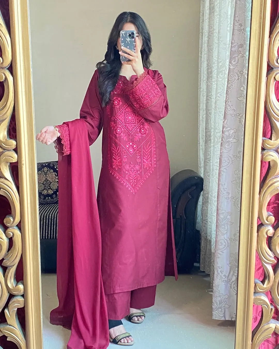 Woman wearing a pink embroidered traditional outfit in front of a decorative mirror.