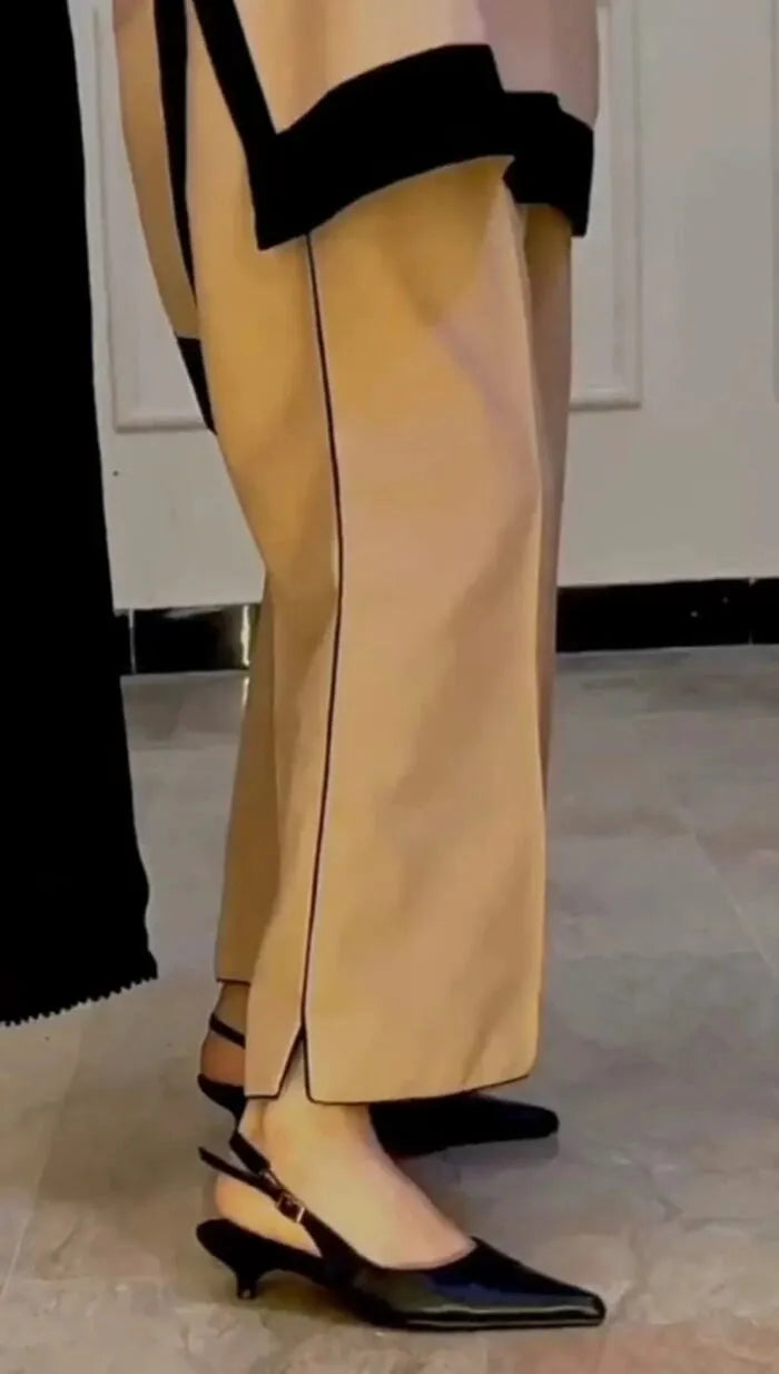 Beige pants with black trim worn by a person, standing on a tiled floor.