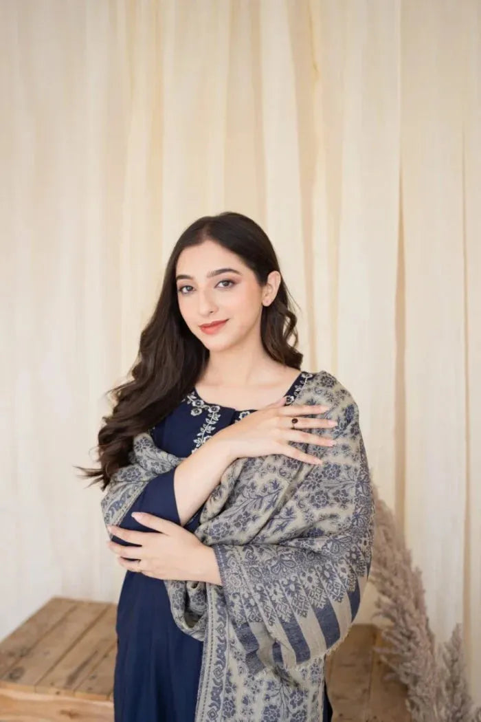 Woman wearing a blue dress with a patterned shawl against a neutral background