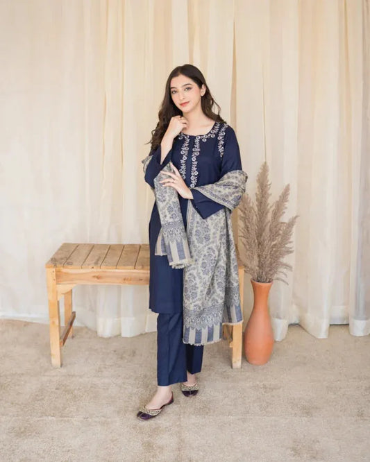 Woman in a navy blue and gray traditional outfit standing next to a wooden bench and decorative vase.