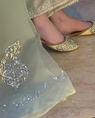 Close-up of a child's feet in gold shoes with a decorative anklet on a wooden floor.