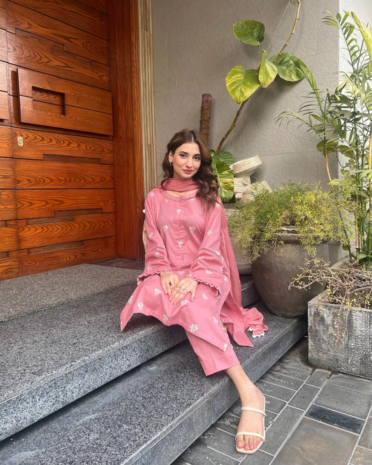 Woman in a pink traditional outfit sitting on steps with plants around.