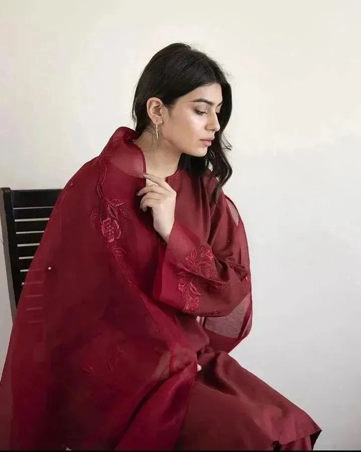 Woman wearing a red traditional outfit with embroidery, sitting against a plain background.