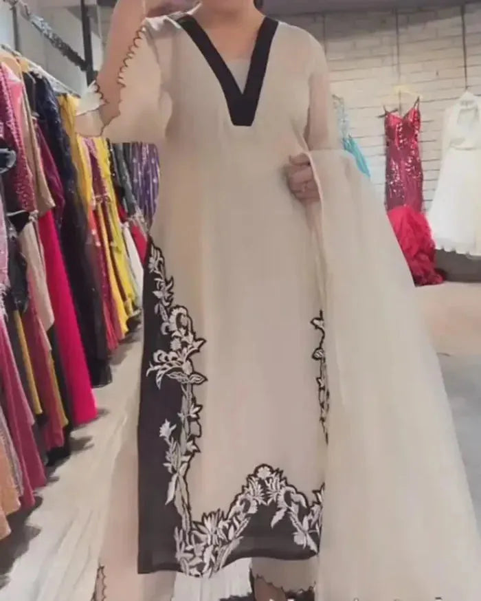 Person wearing a long, light-colored dress with black floral embroidery in a clothing store.