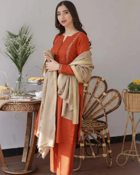 Woman in an orange outfit holding a beige scarf in a room with a table and chairs.