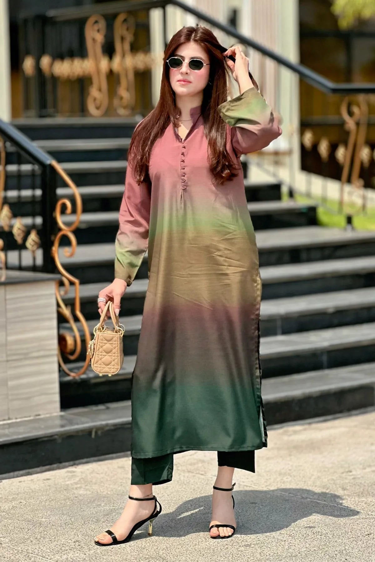 Woman wearing a gradient dress standing outdoors with steps and decorative elements in the background.
