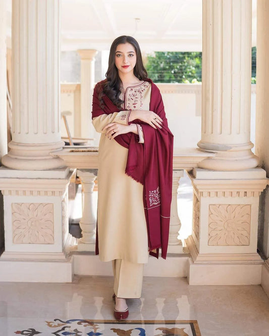 Woman in a cream outfit with a maroon dupatta standing in an elegant interior setting.