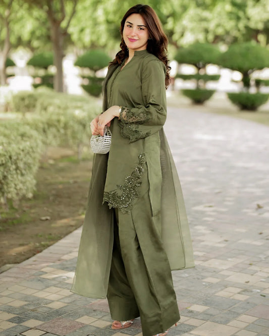 Woman in a green outfit with floral embroidery standing in a park.