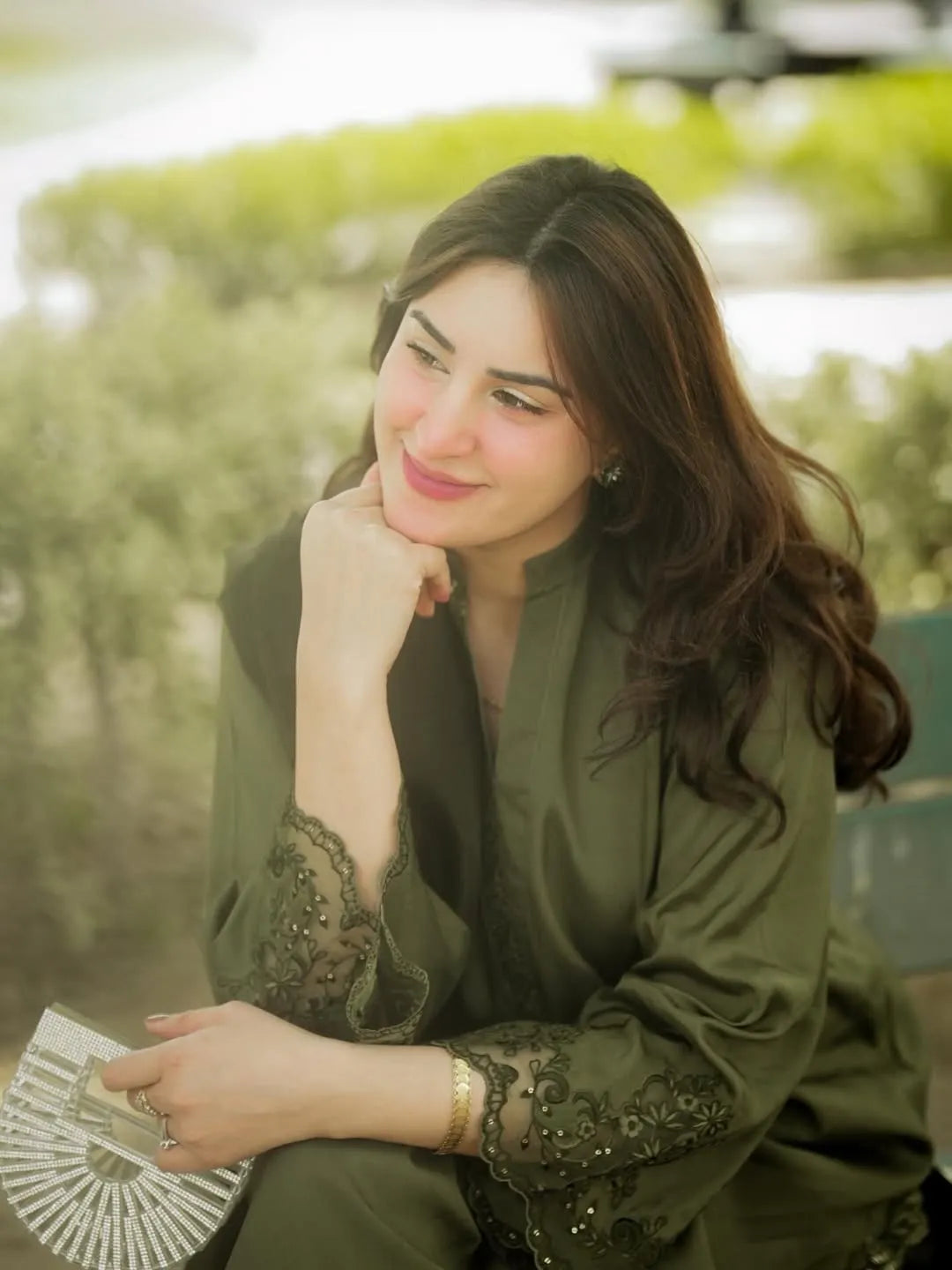 Woman in a green outfit sitting outdoors with trees in the background