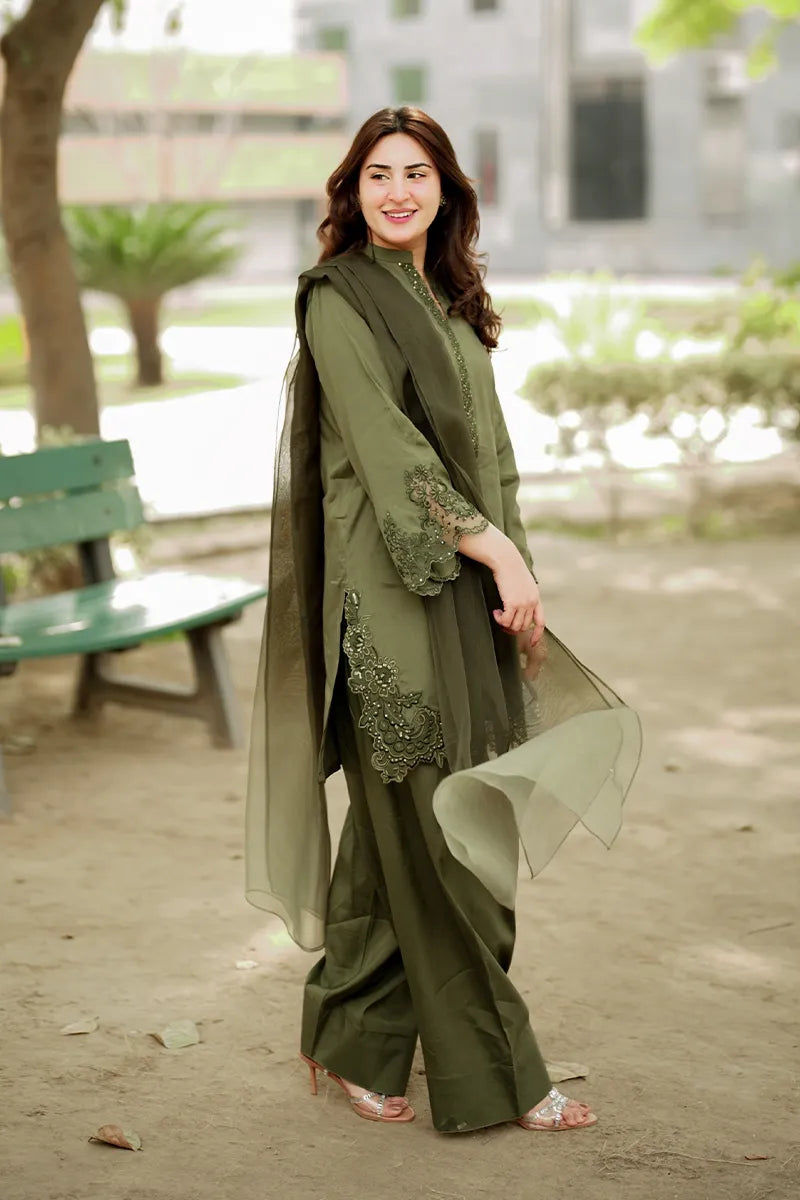 Woman in a green traditional outfit standing outdoors with blurred background
