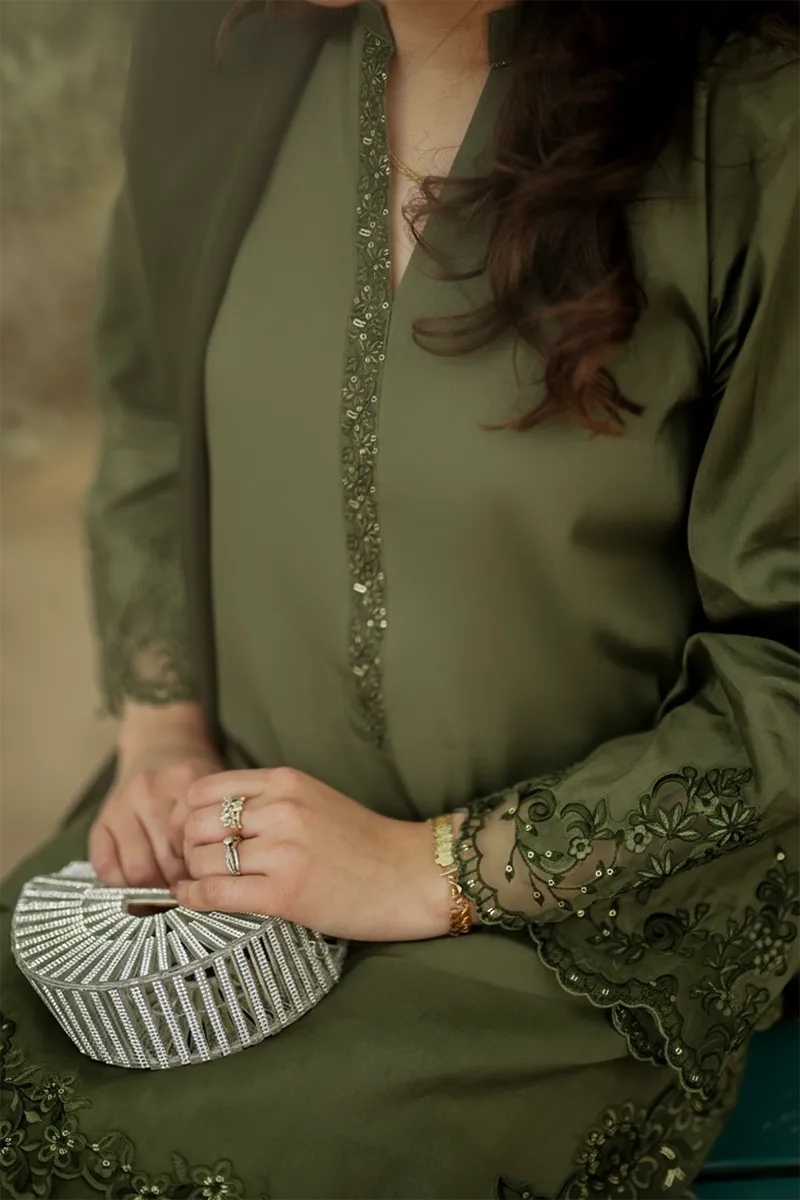 Woman wearing a green embroidered outfit holding a small clutch.