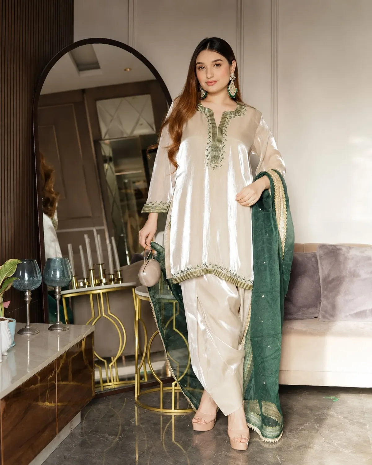 Woman in a white and green traditional outfit standing in a modern living room.