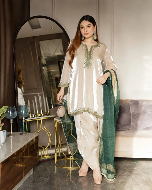 Woman in a white and green traditional outfit standing in a modern living room.